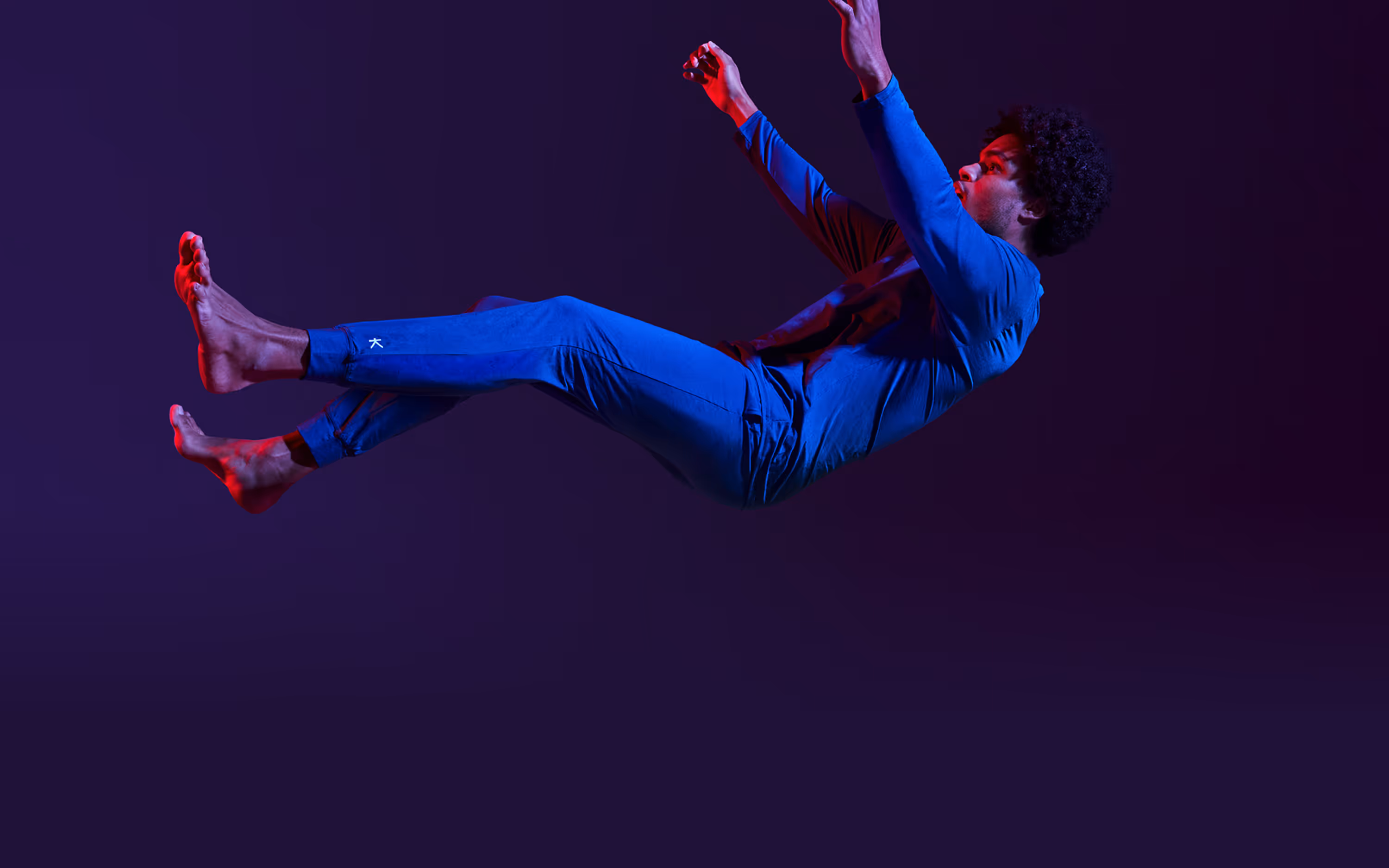 Man in blue outfit floating horizontally against a dark purple background with red lighting highlights.
