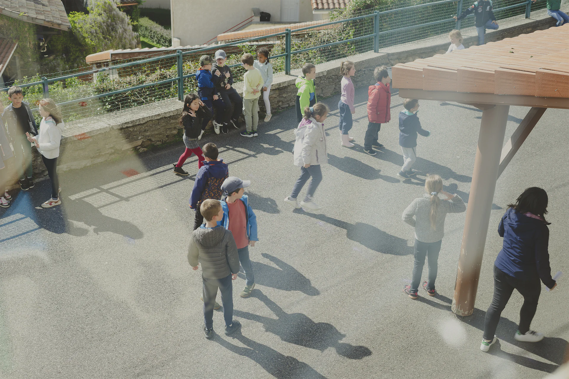 Groupe d'enfants jouant et discutant dans une cour d'école extérieure sous un ciel ensoleillé.