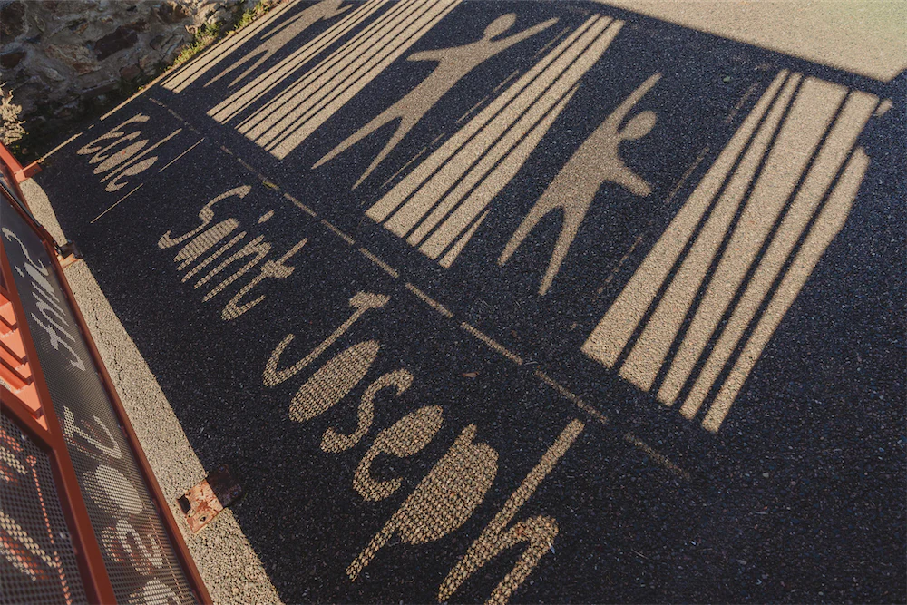 Ombres projetées sur le sol montrant des silhouettes humaines derrière des barreaux et le texte 'École Saint Joseph'.
