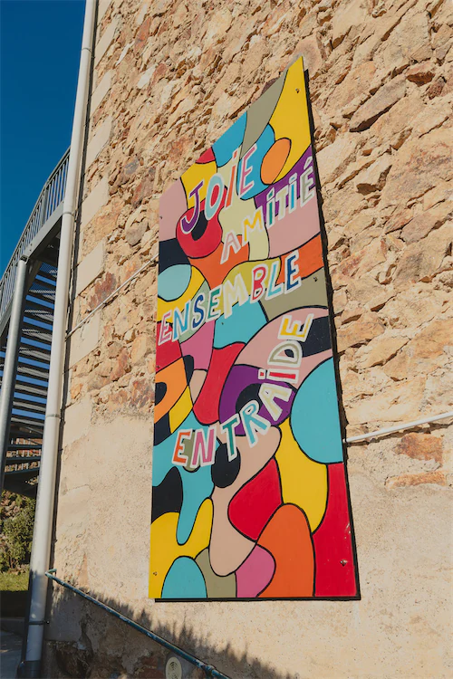 Panneau coloré sur un mur en pierre avec les mots français Joie, Amitié, Ensemble, Entraide.