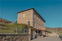 Bâtiment scolaire de l'École de Saint-Joseph en pierre avec ciel bleu et collines en arrière-plan.