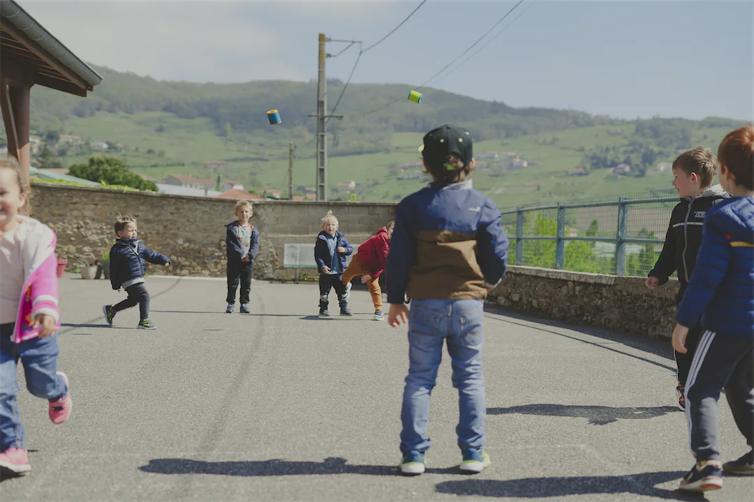 Enfants jouant dehors sur une cour d'école avec une colline verte en arrière-plan.