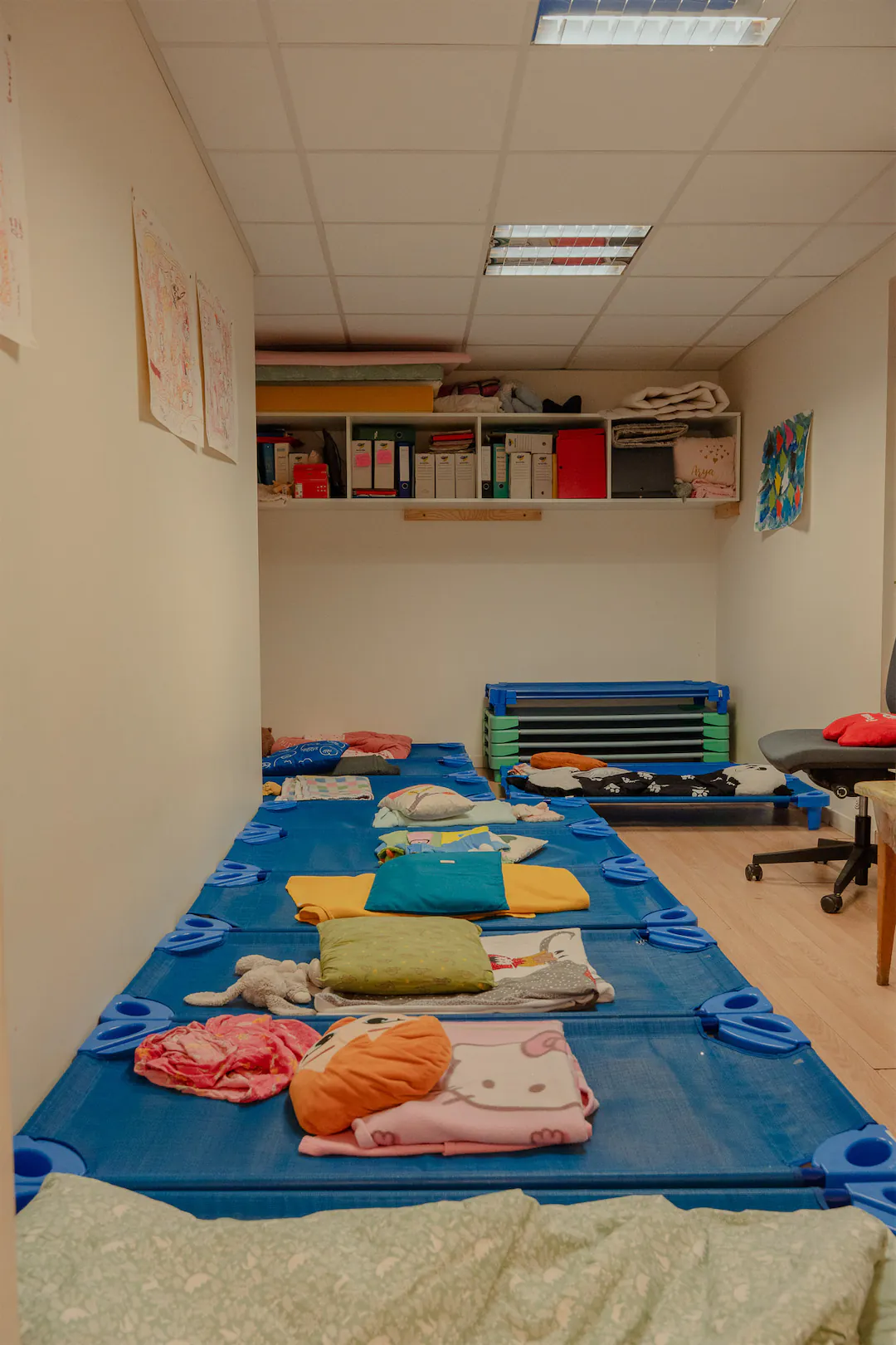 Salle de repos avec des lits d'enfant bleus alignés, couverts de couvertures et de coussins colorés.