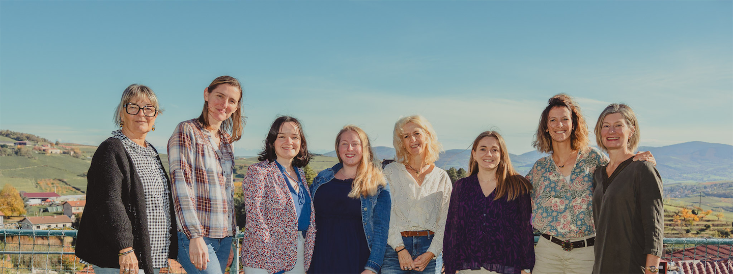 Ensemble de l'équipe pédagogique de l'école Saint-Joseph, souriantes debout côte à côte en plein air avec un paysage de campagne en arrière-plan.