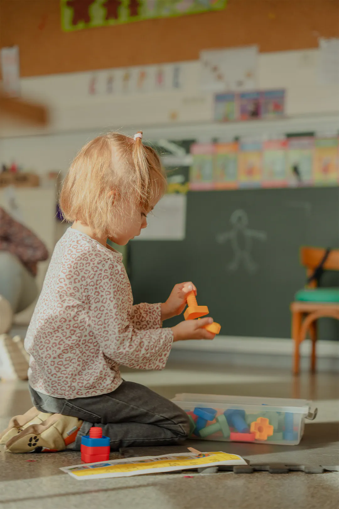 Jeune enfant assise par terre dans une salle de classe, jouant avec des blocs de construction colorés.