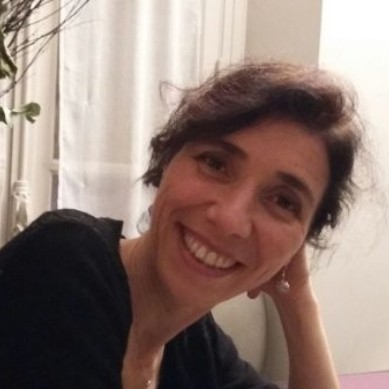 Smiling woman with dark hair resting her head on her hand indoors.