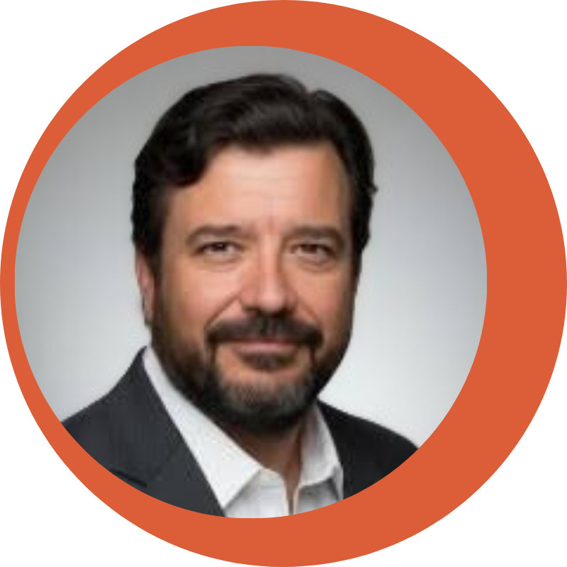 Headshot of a middle-aged man with dark hair and beard, wearing a dark suit jacket and white shirt against a neutral background.