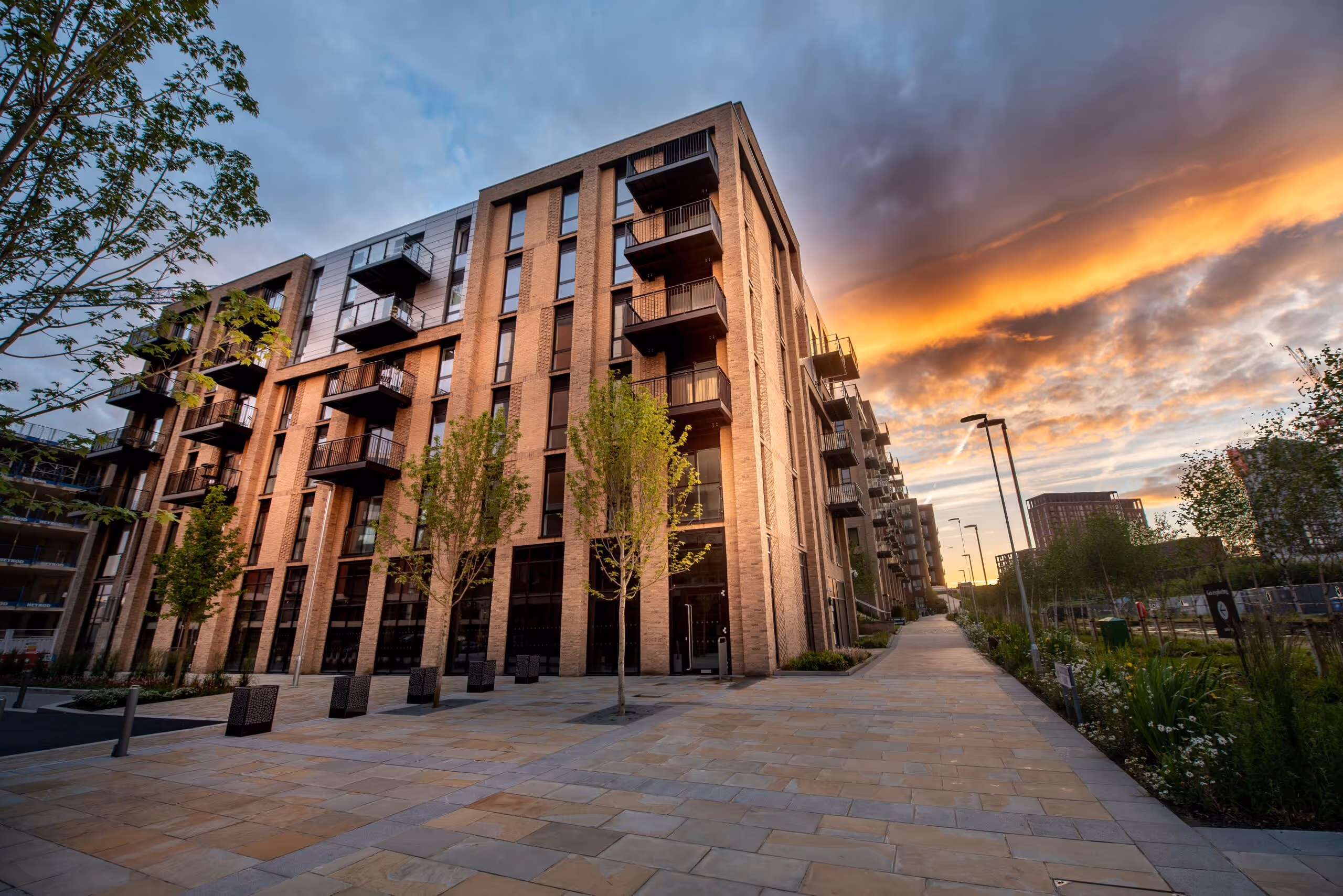 Modern apartment building with balconies at sunset under a partly cloudy orange and blue sky.
