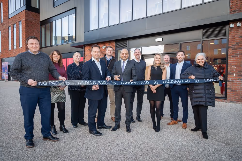 Group of people standing outside a modern building holding a black ribbon with 'Landing Pad' text for a ribbon-cutting ceremony.
