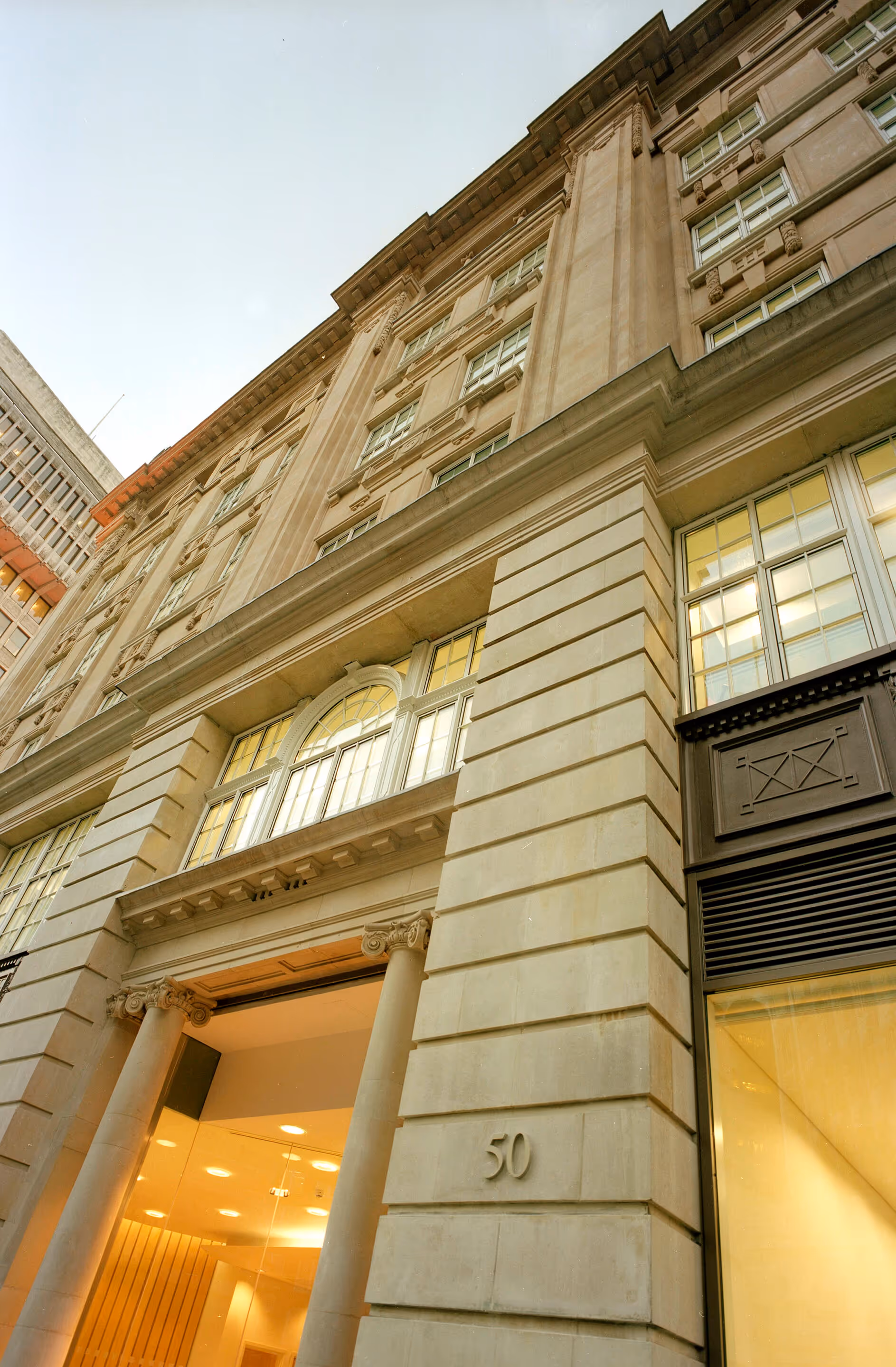 Upward view of a beige stone building with classical columns and the number 50 carved on the facade.
