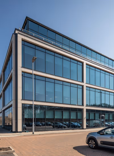 Modern three-story office building with large blue-tinted glass windows under a clear sky, with parked cars in front.