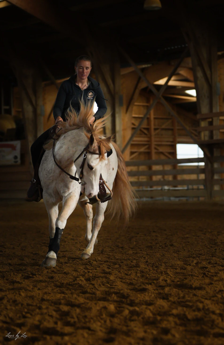 Une femme monte un cheval blanc avec une crinière rousse dans une écurie.