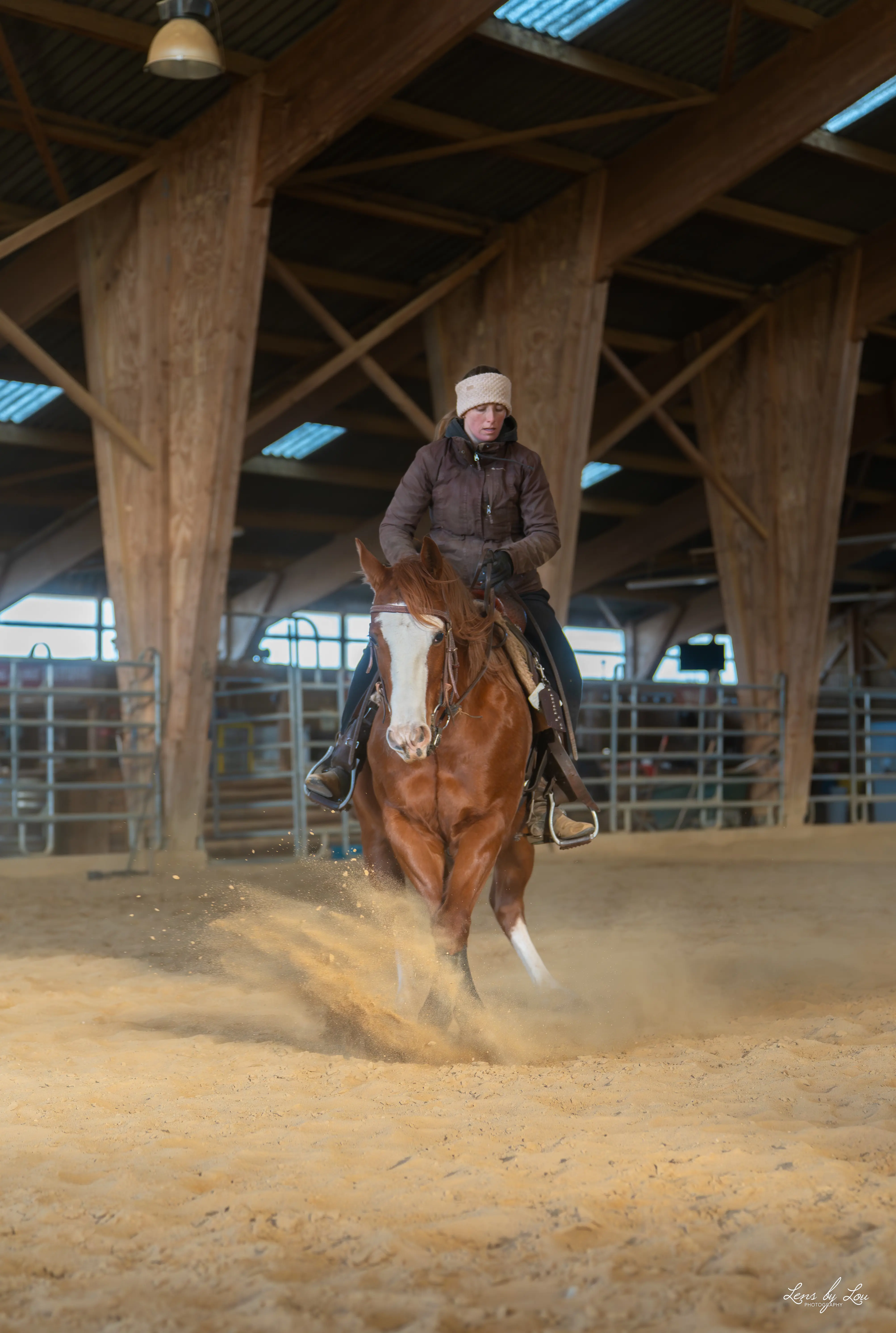 Cavalière en tenue d'hiver exécutant un arrêt brusque sur un cheval alezan dans une carrière couverte en bois.