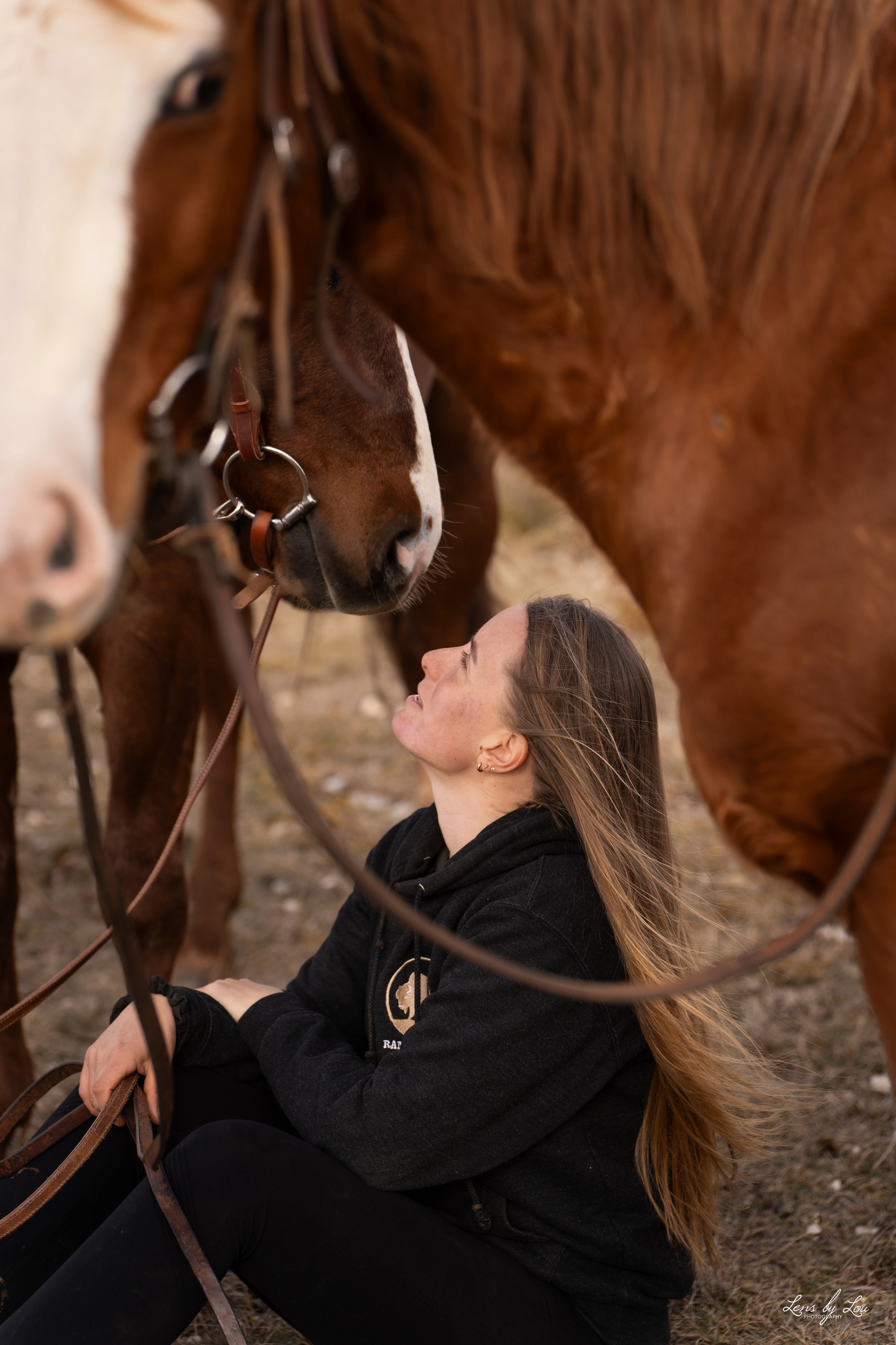 Femme assise sur le sol regardant affectueusement un cheval marron avec une bride.