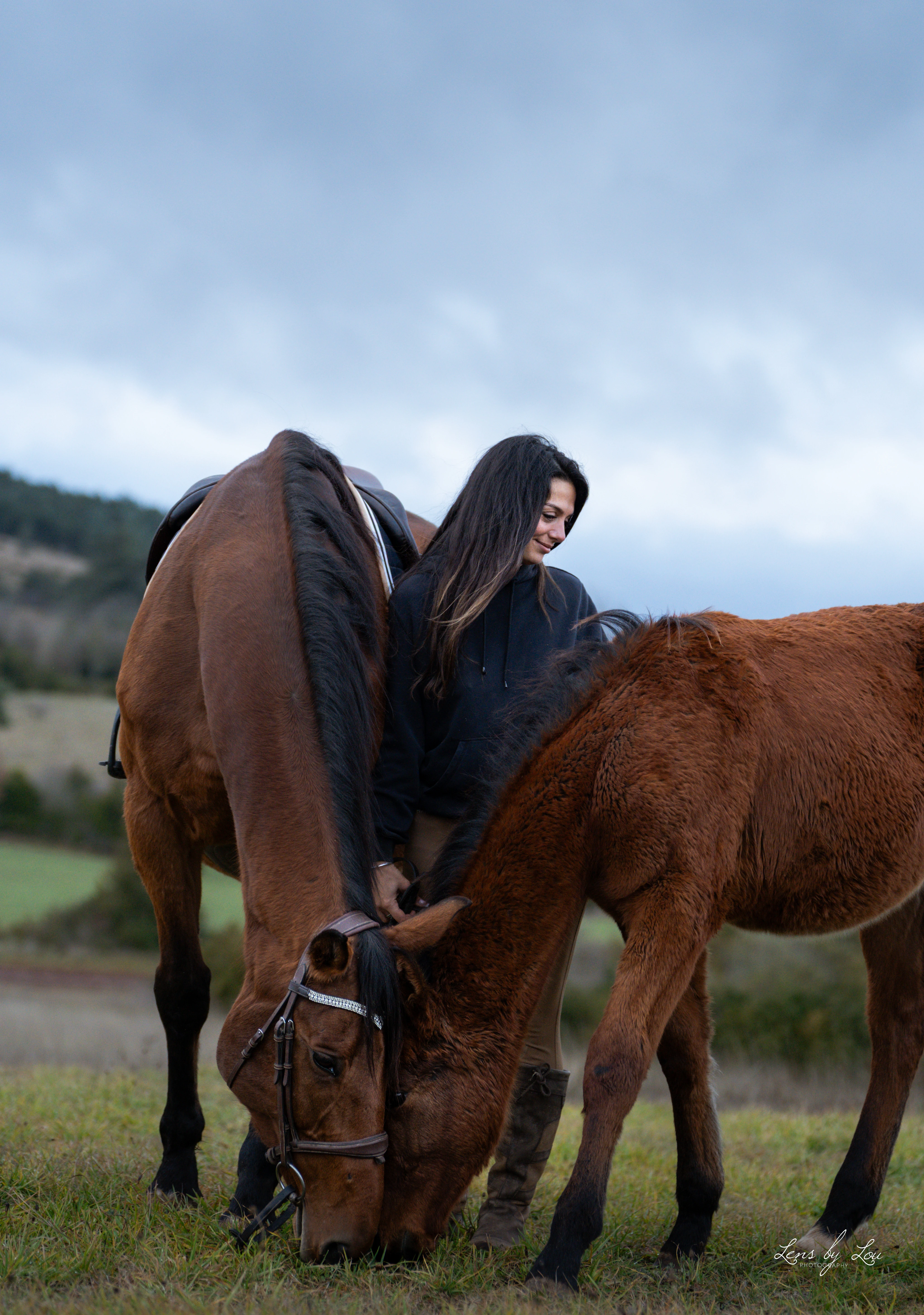 Femme assise sur le sol regardant affectueusement un cheval marron avec une bride.