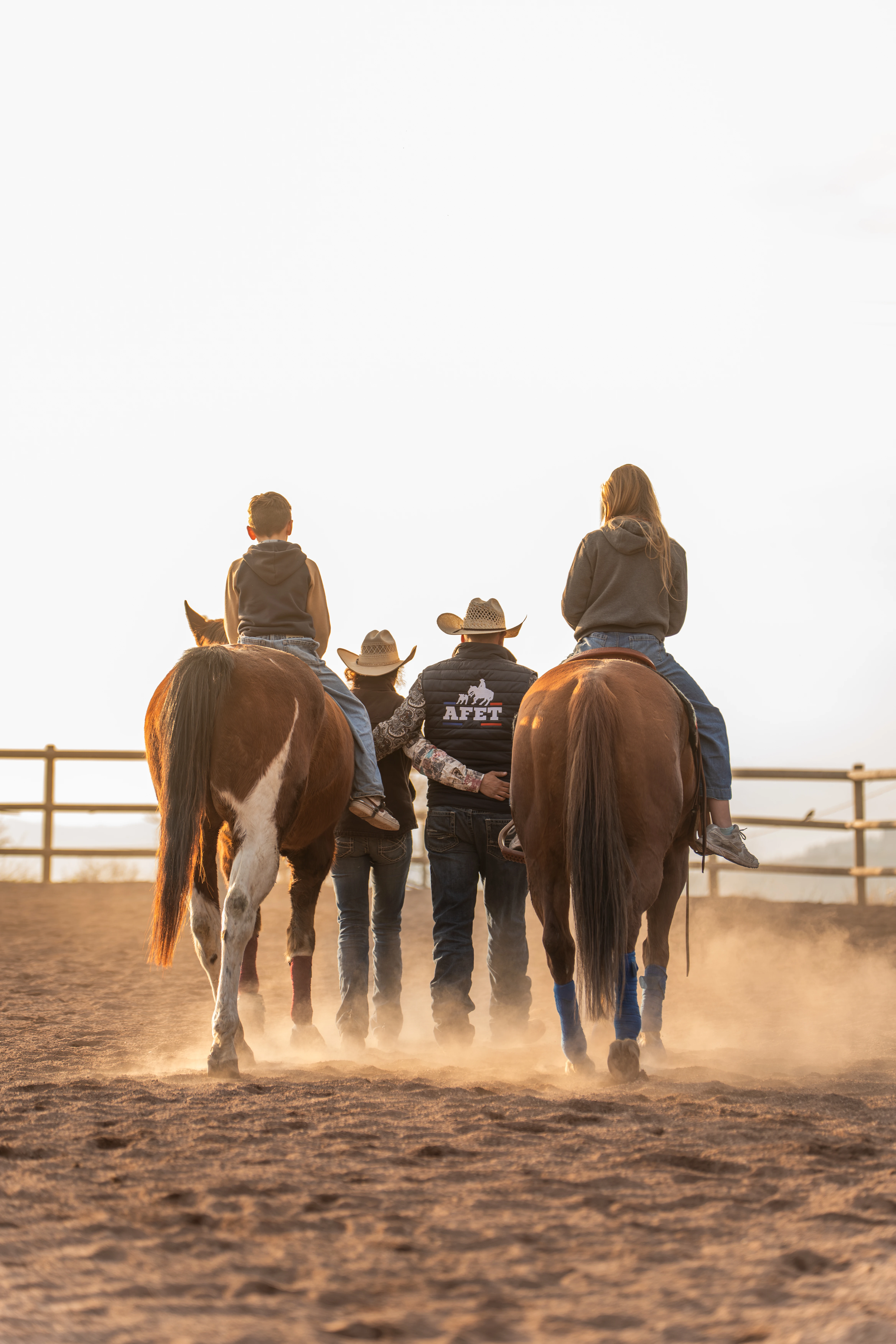 Femme en tenue équestre caressant un cheval noir qui broute dans une écurie, à côté d'un autre cheval marron.