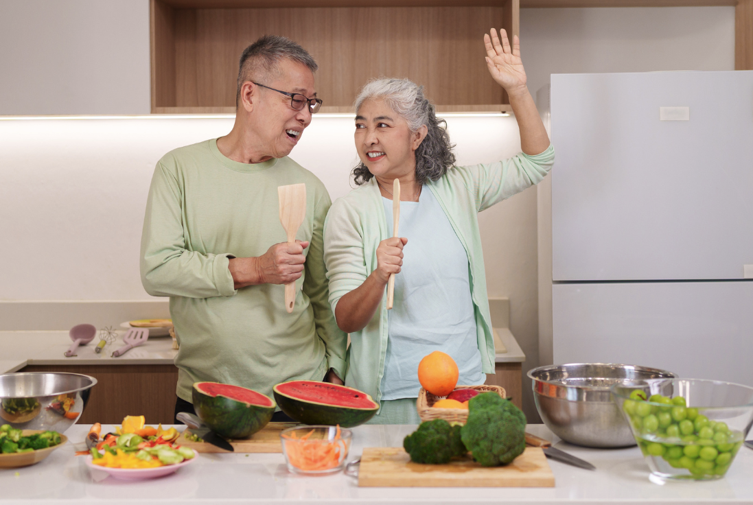 A older couple in the kitchen singing while they work