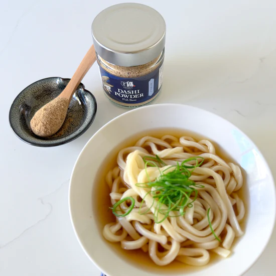Gozen Dashi Fish Based jar on bench next to udon bowel, dish with spoon and powder