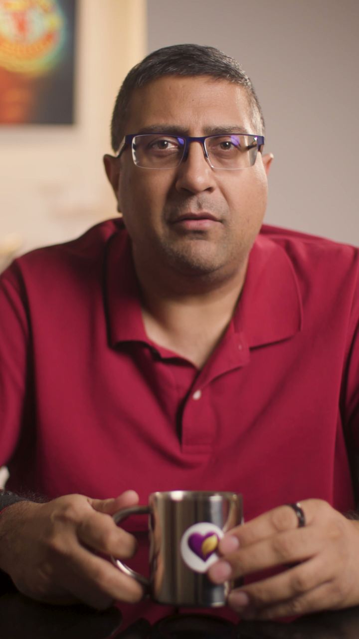Paraag Amin at his desk in a red shirt, holding a mug and looking into the camera