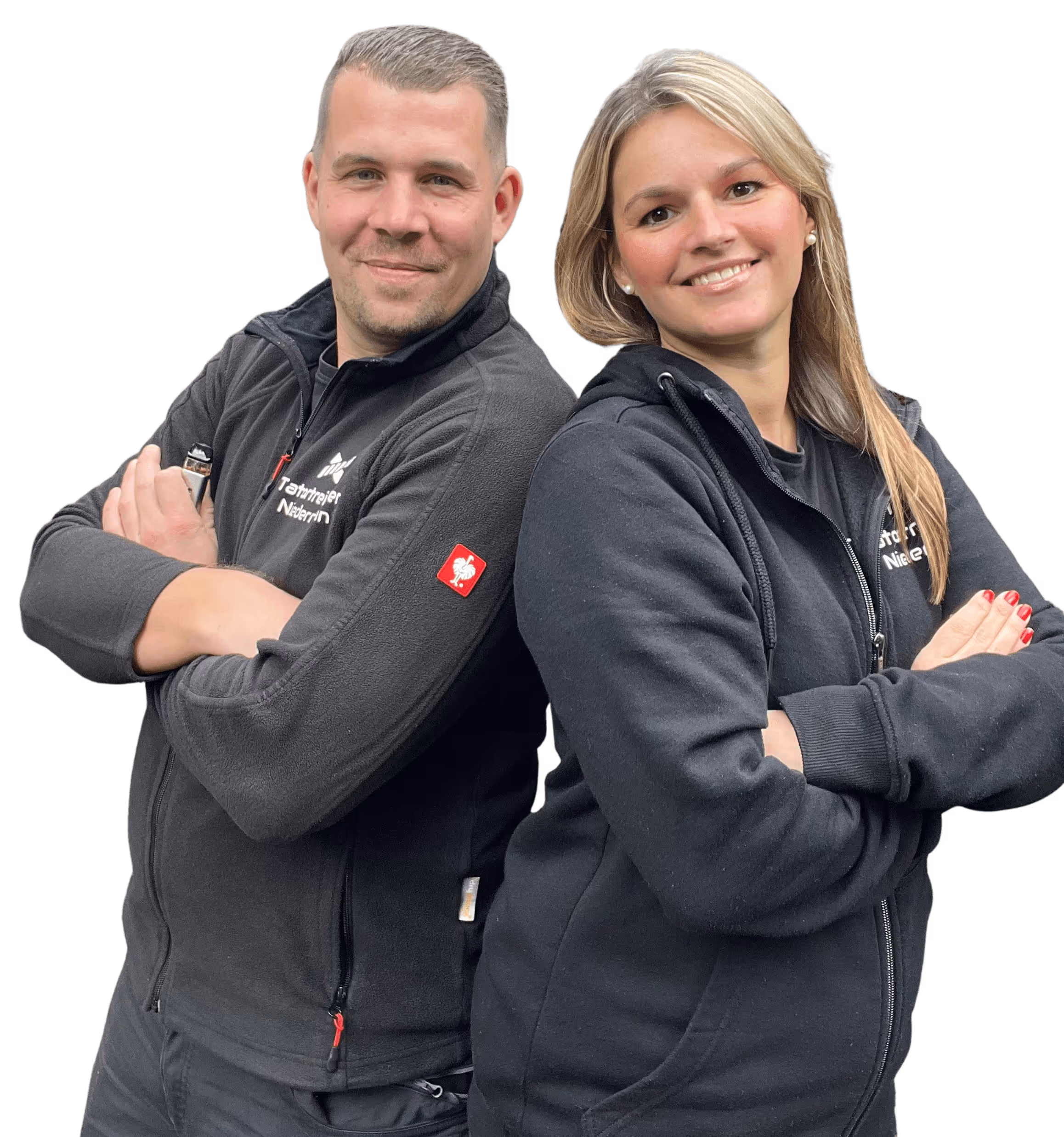 Zwei lächelnde Personen, ein Mann und eine Frau, stehen Rücken an Rücken mit verschränkten Armen, beide tragen schwarze Jacken.