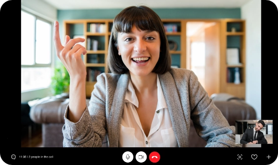 Smiling woman with short brown hair and a gray blazer raising her hand during a video call in a well-lit room.