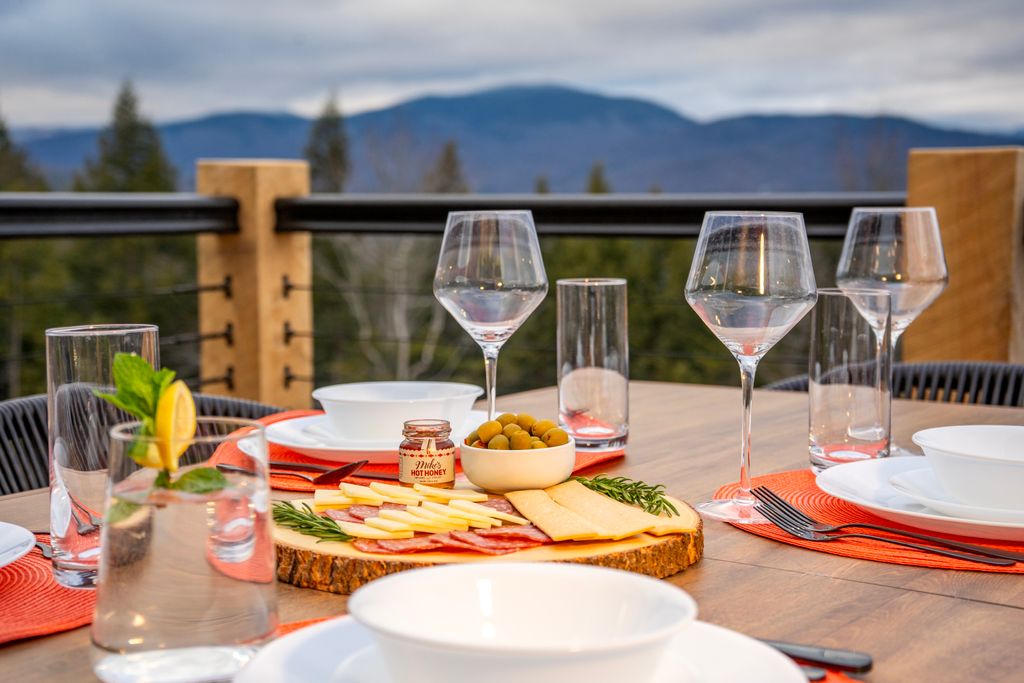 Outdoor dining table on a mountain-view deck in Bethel, Maine with wine glasses and shared plates