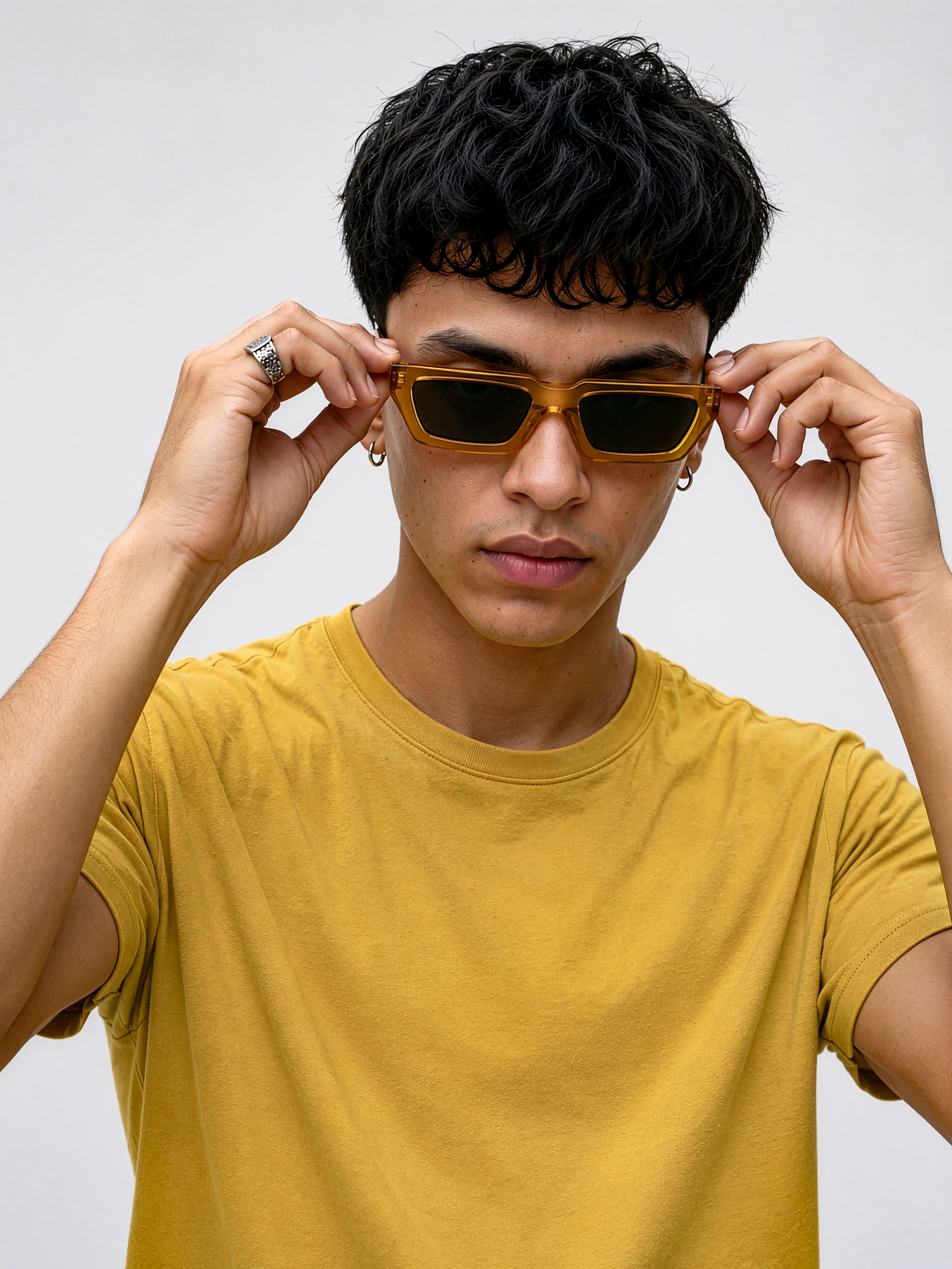Jeune homme portant un t-shirt jaune ajustant ses lunettes de soleil à monture jaune transparente.