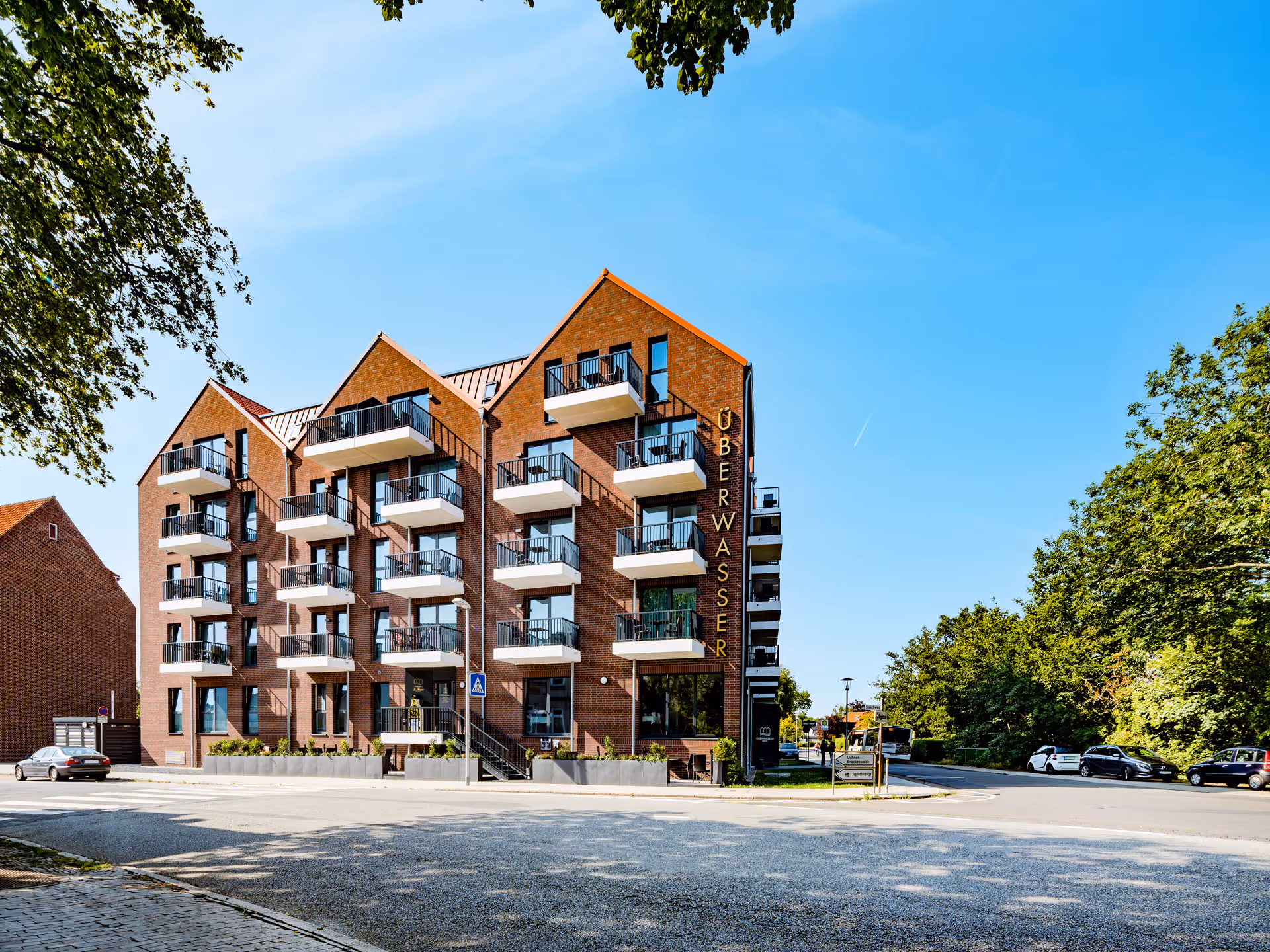 Mehrstöckiges modernes Wohngebäude aus rotem Backstein mit mehreren Balkonen bei klarem Himmel.