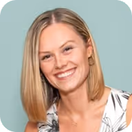 Smiling woman with straight blonde hair wearing a patterned sleeveless top against a pale blue background.