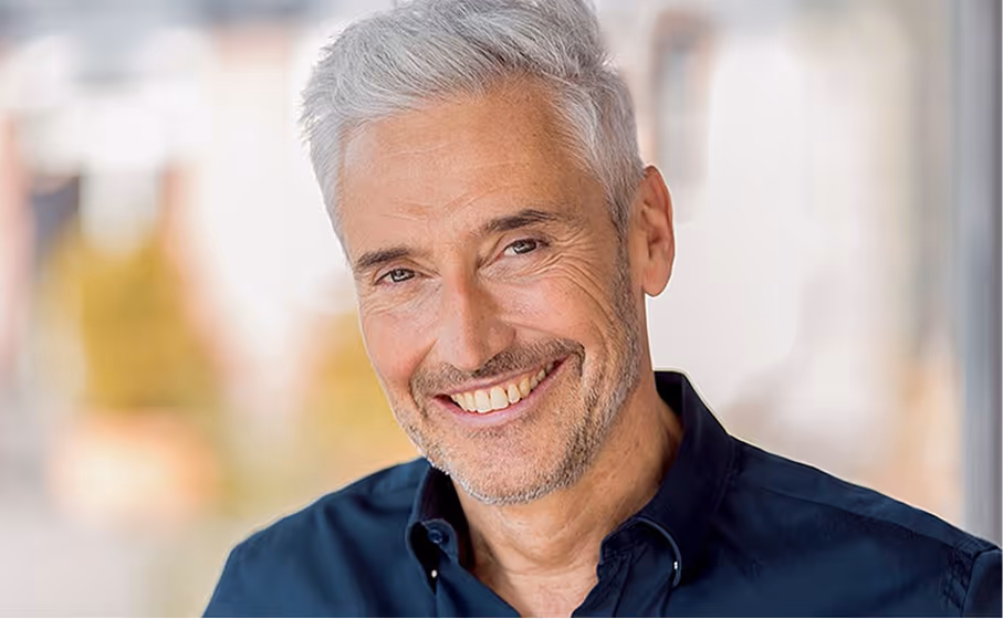 Smiling middle-aged man with gray hair and stubble wearing a dark blue shirt.