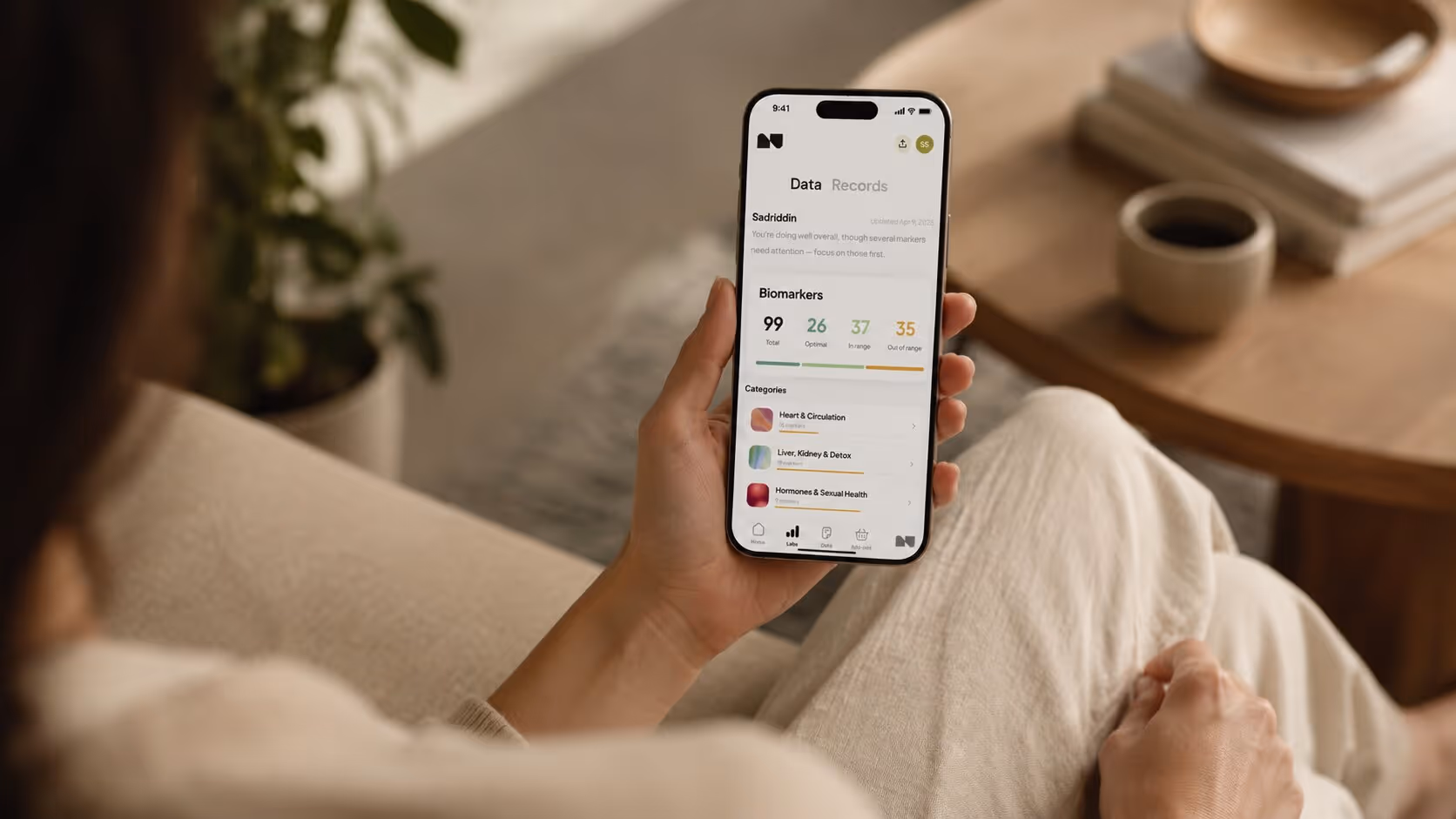 Person holding smartphone displaying health app with biomarker data and health categories.
