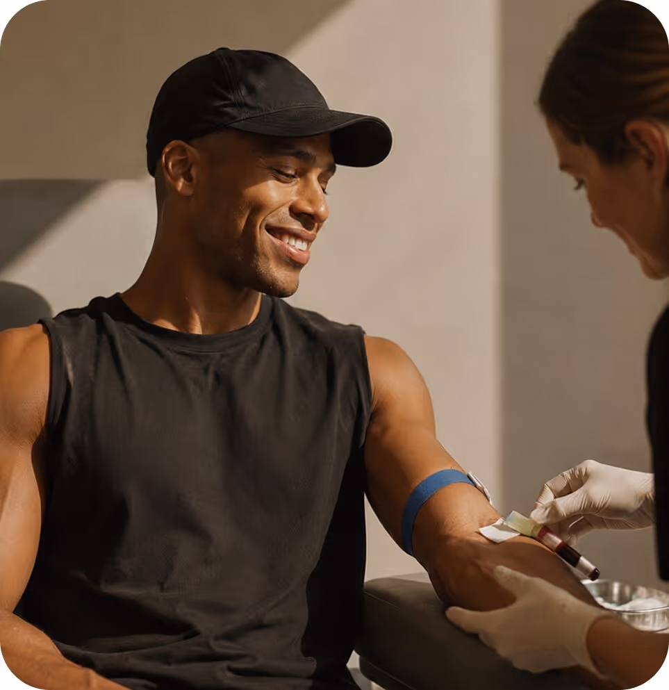 Man smiling while a healthcare worker draws blood from his arm with a tourniquet applied.
