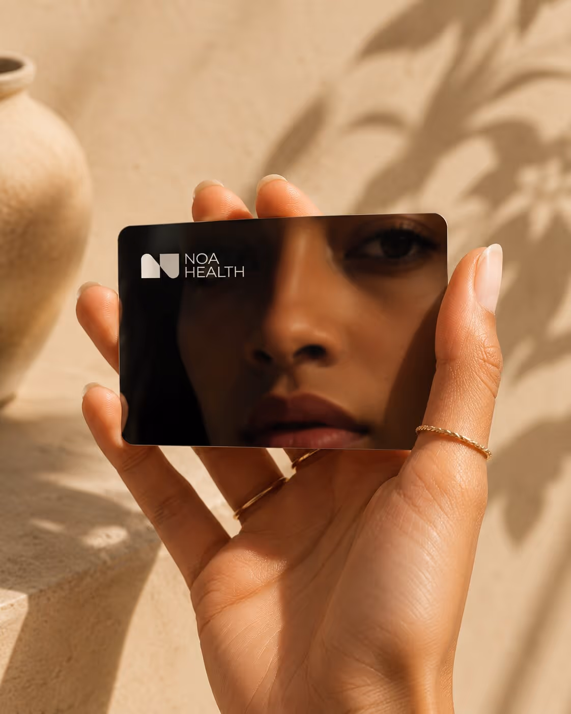 Hand holding a reflective black card with NOA Health logo and a face reflected on it.