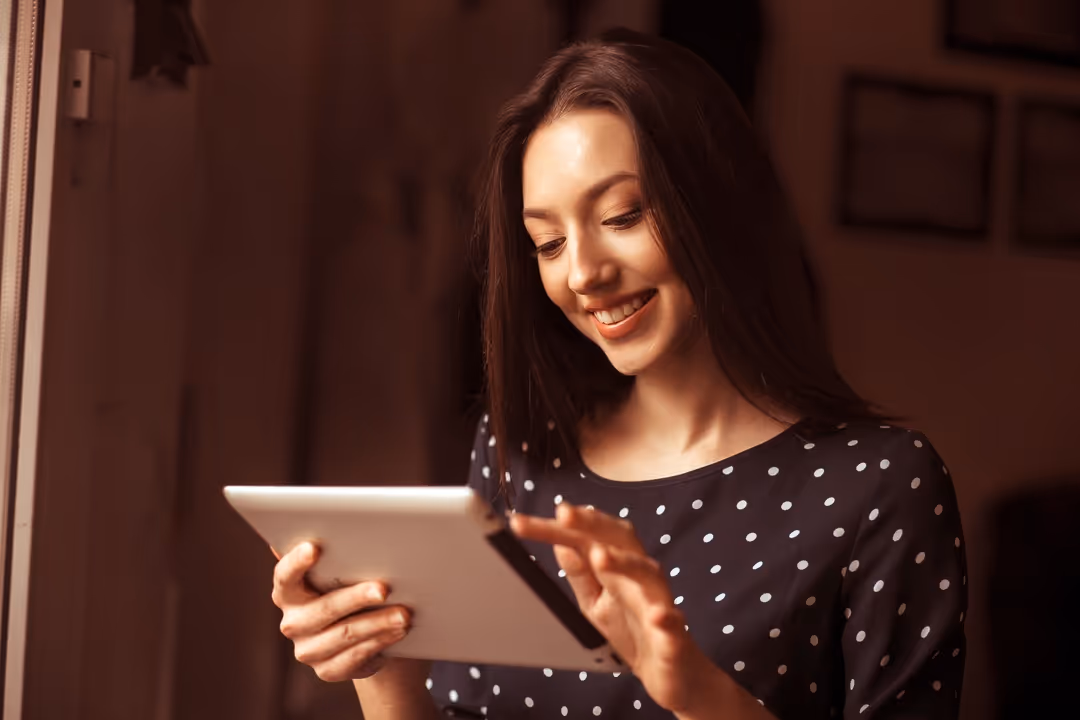 Mulher sorridente usando um tablet branco em ambiente interno iluminado.