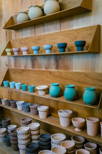 Wooden shelves displaying rows of small colorful ceramic pots and cups in pastel and earthy tones.