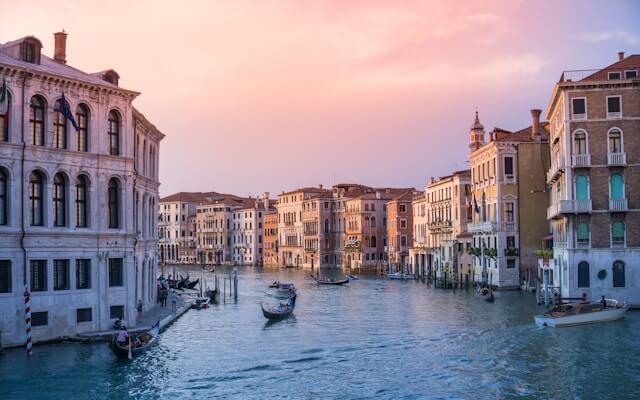 Gondolas floating on a canal surrounded by historic buildings at sunset in Venice, Italy.