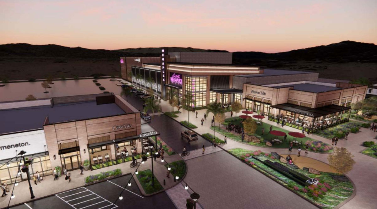 Aerial view of a modern shopping and dining complex at dusk with pedestrian walkways, outdoor seating areas, landscaped gardens, and lit storefronts including Casa Mia and a megaplex theater.