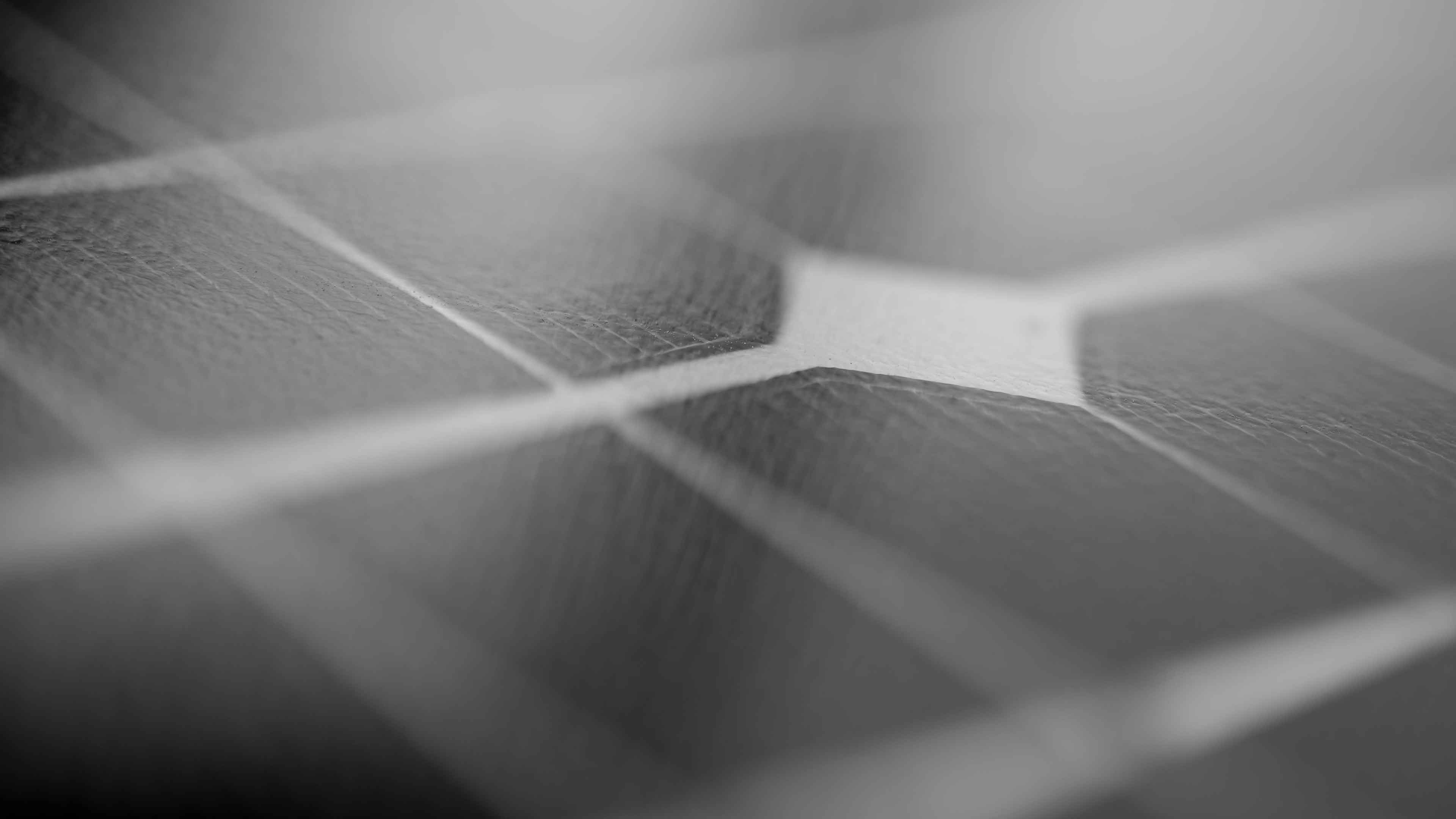 Close-up of a solar panel surface showing its textured solar cells and grid lines in black and white.