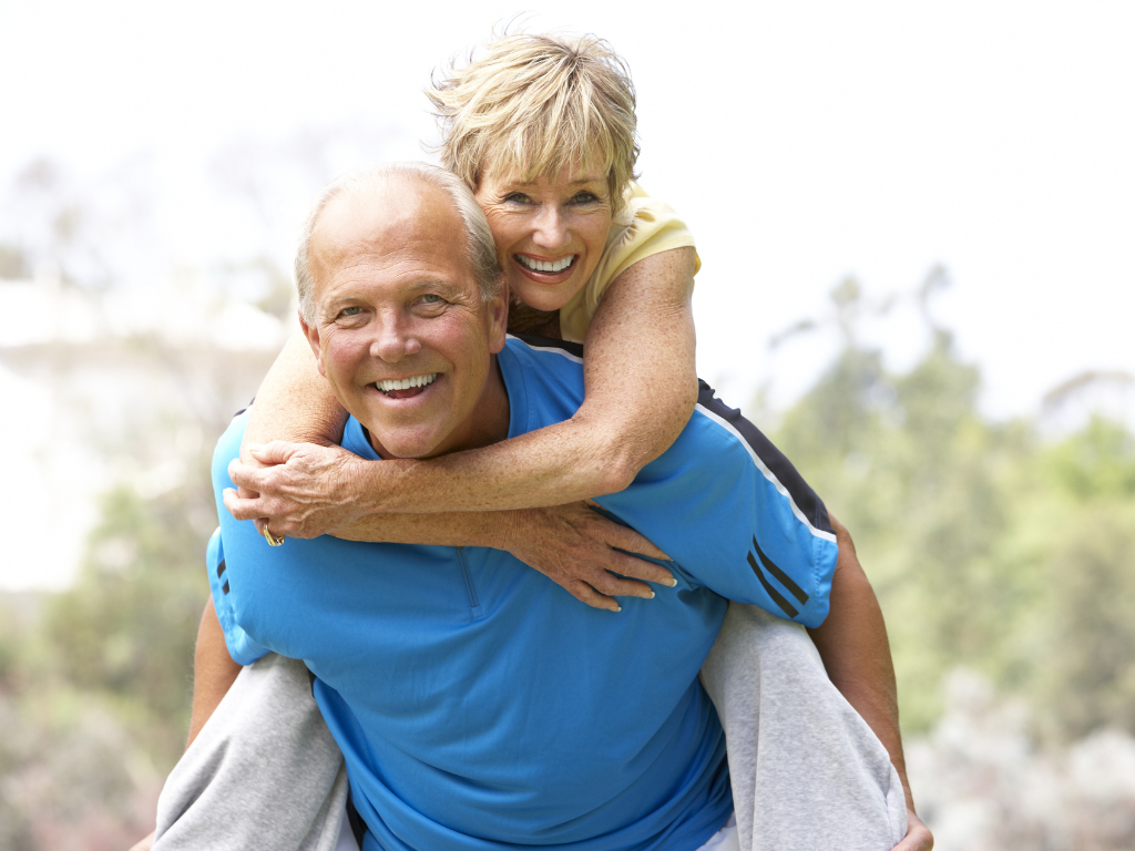 Smiling senior woman giving a piggyback ride to a smiling senior man outdoors.