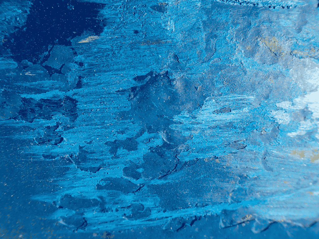 Close-up of a textured blue surface with uneven patches and streaks resembling peeling paint or weathered material.