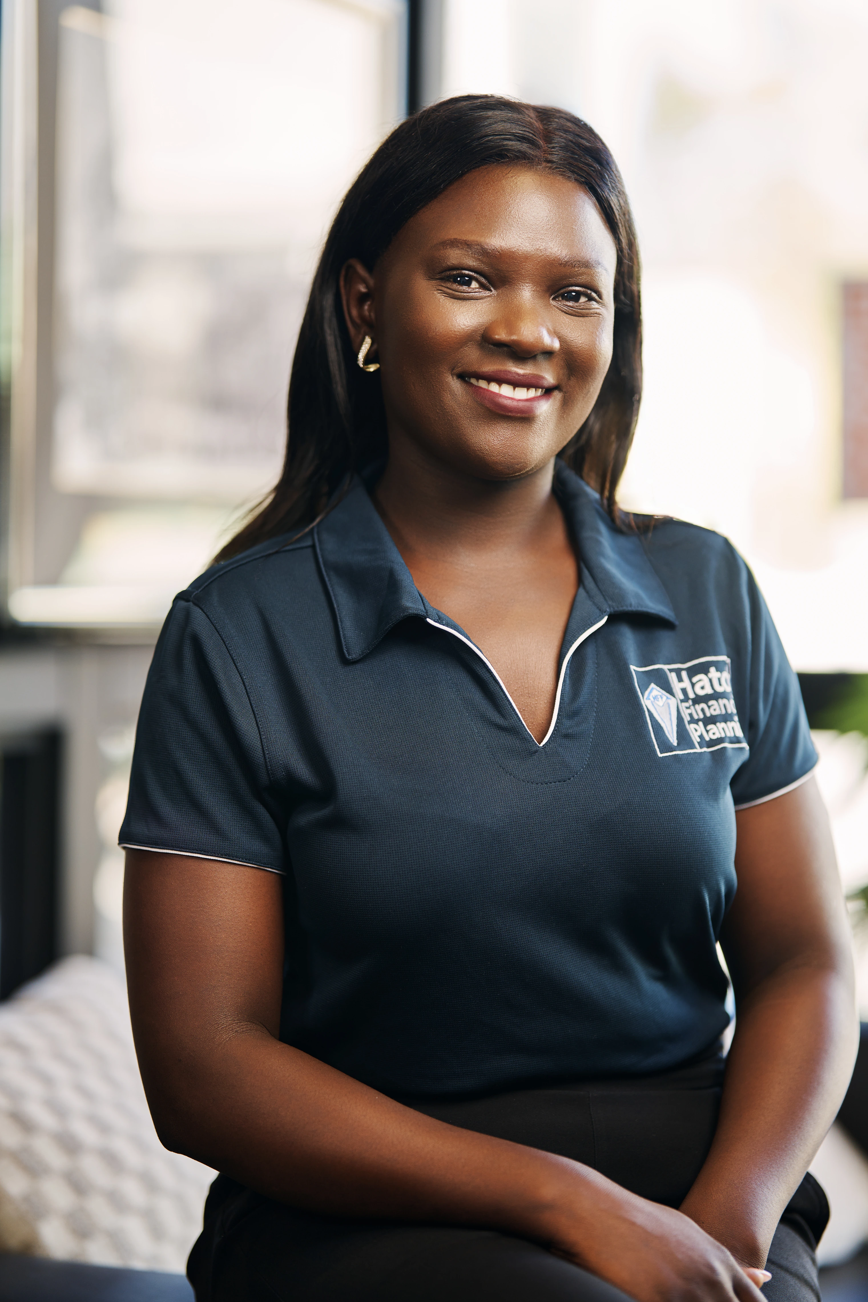 Smiling woman wearing a navy blue Hatch Financial Planning polo shirt seated indoors.
