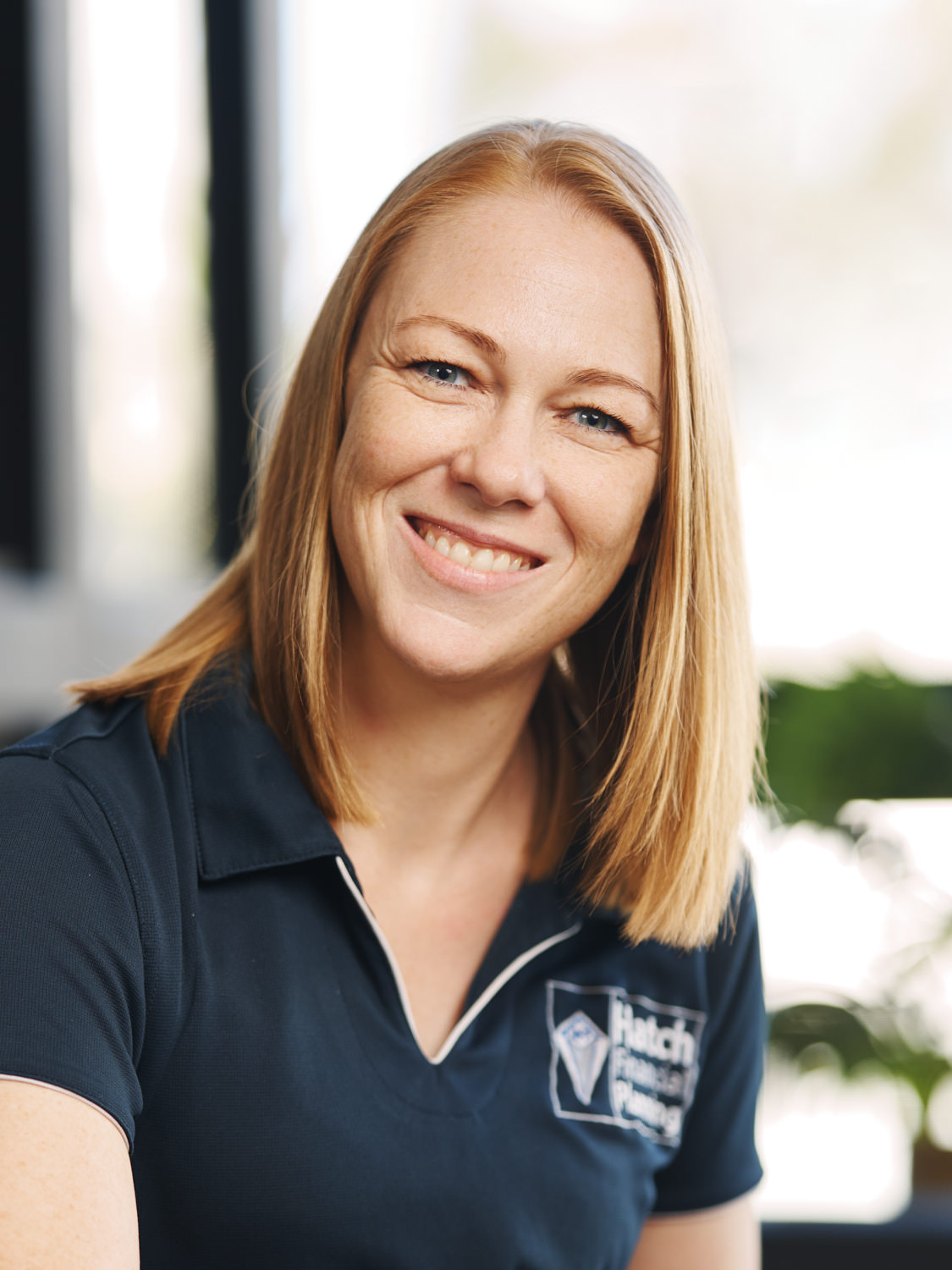 Smiling woman with straight shoulder-length blonde hair wearing a navy polo shirt with a Hatch Physical Therapy logo.