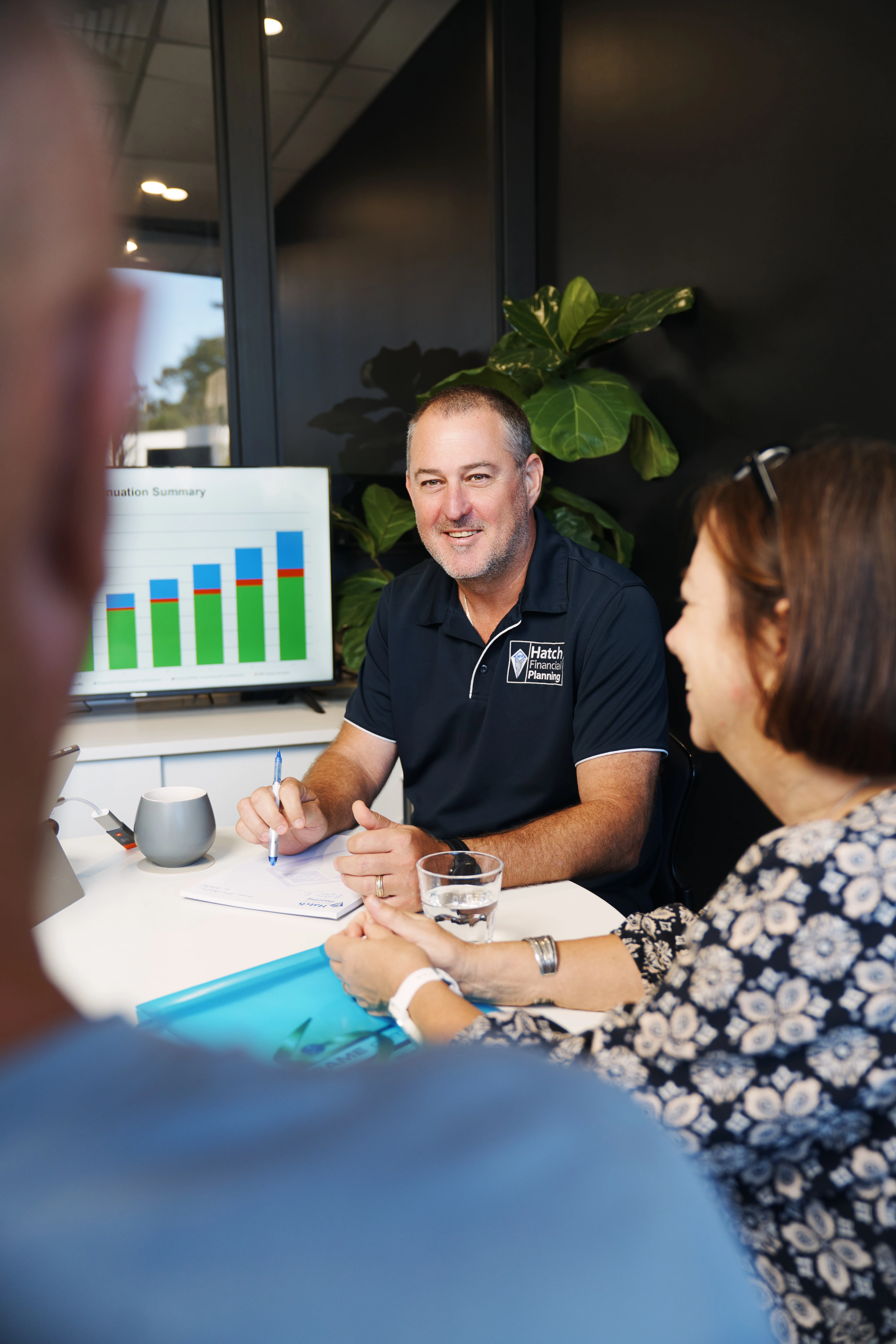 Financial advisor in a navy blue shirt consulting a couple with a bar chart displayed on a monitor in the background.