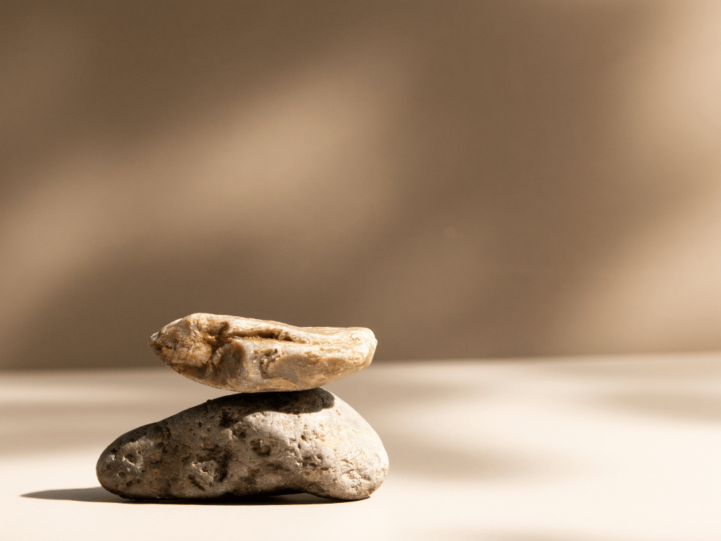 Two balanced natural stones stacked on a smooth surface with a blurred brown background.