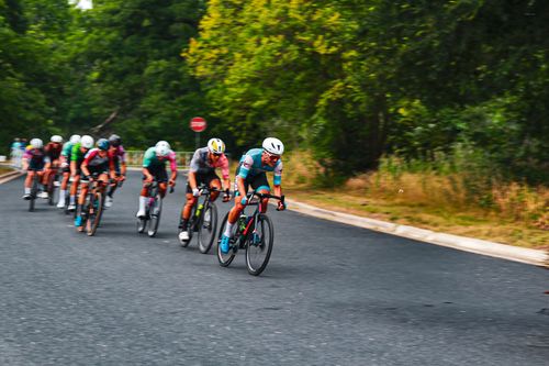Cyclists racing on a paved road surrounded by greenery during a cycling competition.