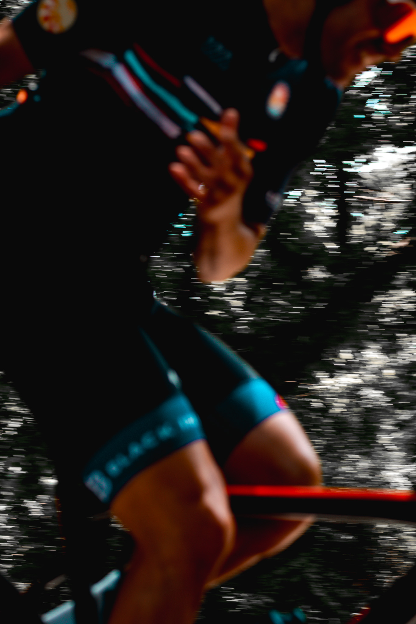 Close-up of a cyclist in motion wearing a black and blue racing outfit, with blurred trees in the background.