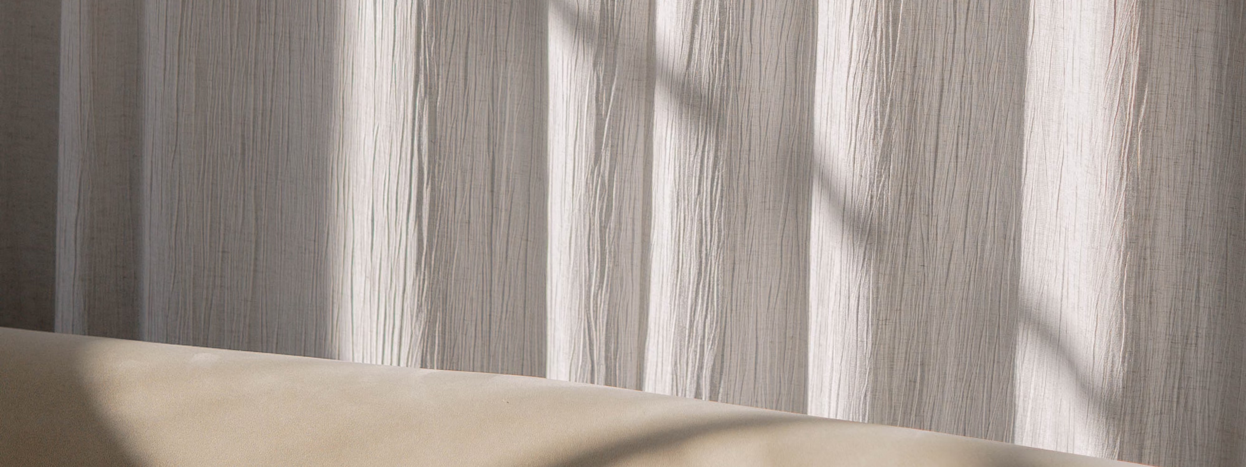 Soft sunlight casting shadows on a textured white curtain above a beige surface.