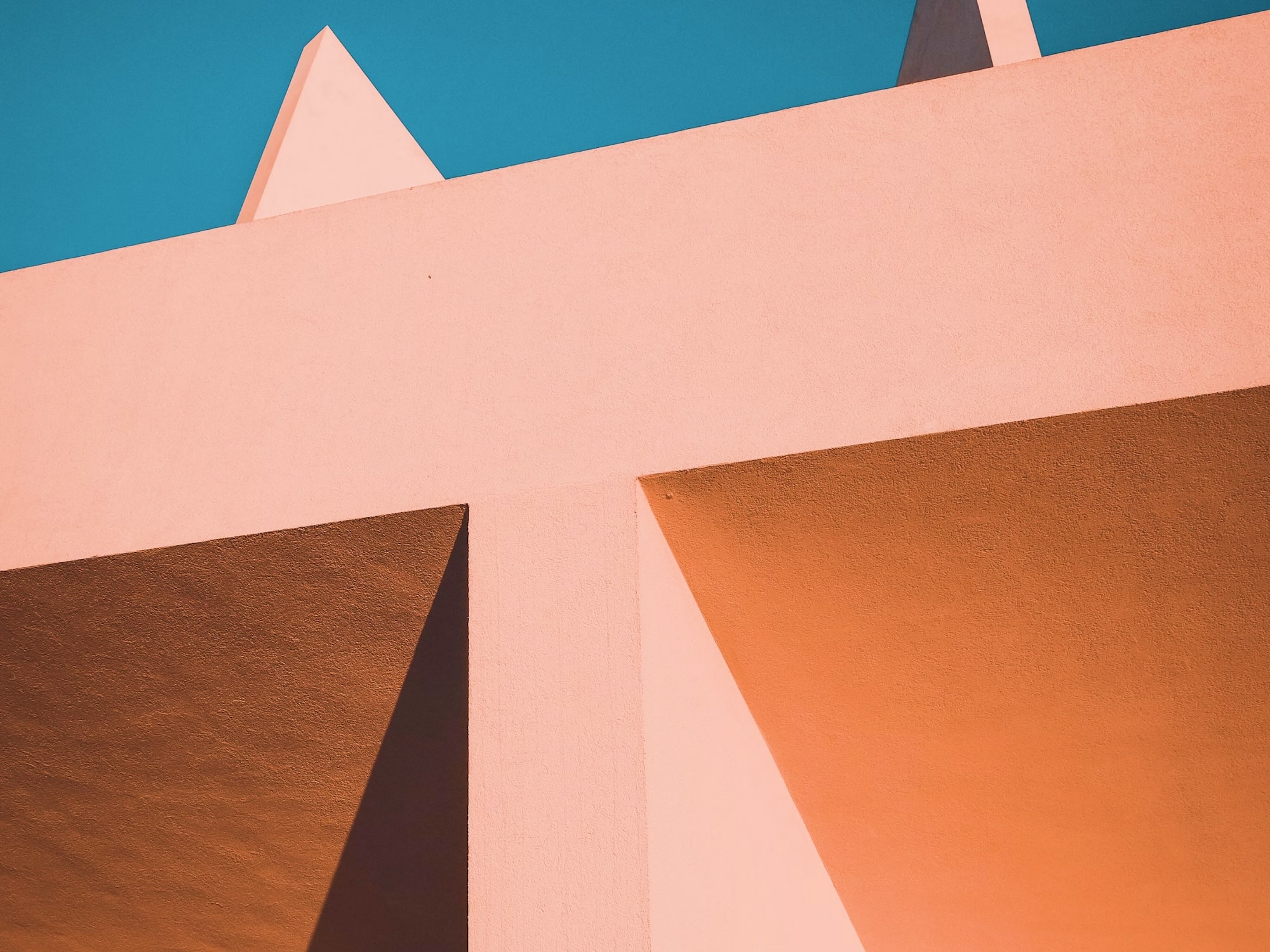 Close-up of a modern architectural structure with peach-colored walls, sharp angles, and a blue sky background.