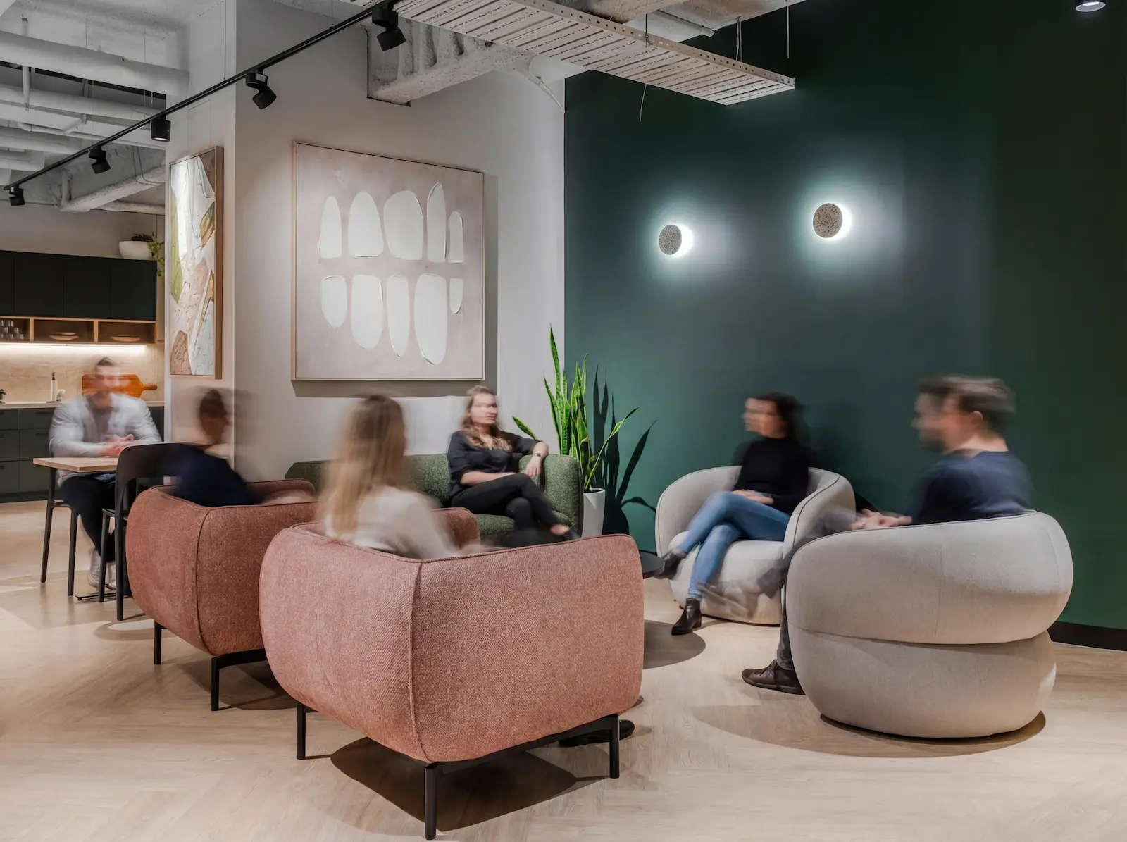 Modern office lounge with six people sitting in armchairs and sofas, blurred motion, and abstract wall art.