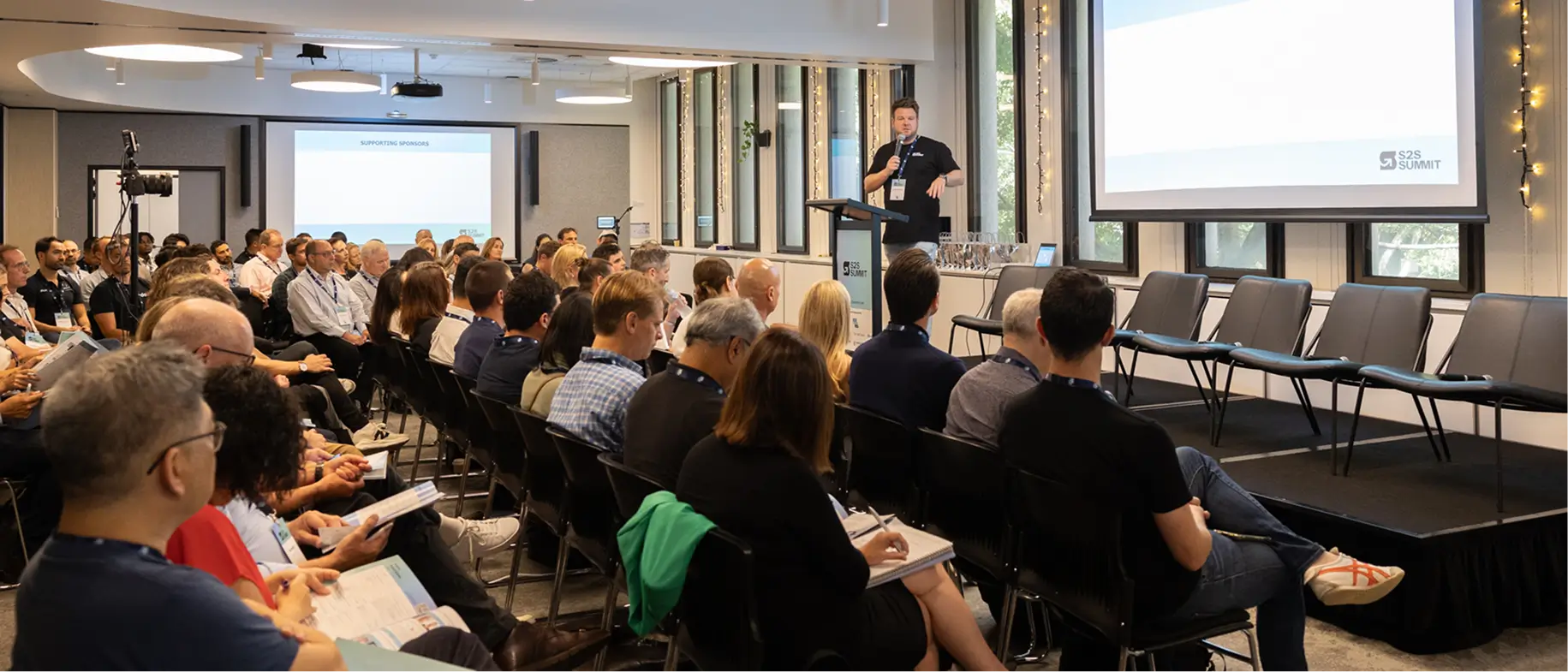 Man speaking on stage to an attentive audience seated in rows during a conference or summit.